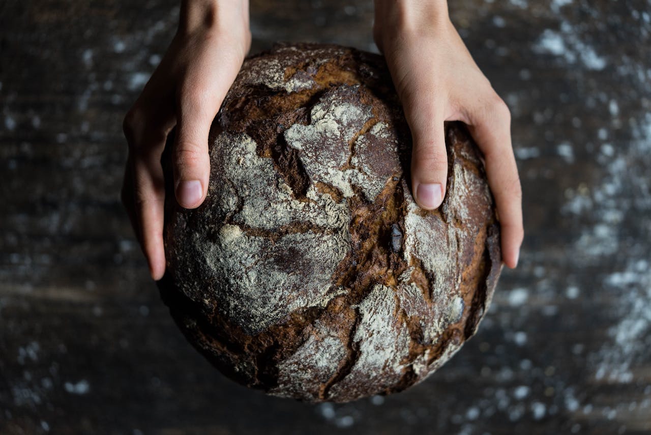 The Art of Drawing Readers In: Your attractive post title goes here Close-up of hands holding a rustic loaf of whole wheat bread with a dark, textured crust.